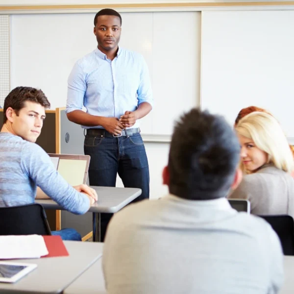 College students in a classroom setting, with one student standing and addressing the group representing full-time students discussing how to balance CFA exam prep with academic classes.